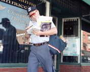 Postal Carrier walking with mail in front of a glass storefront