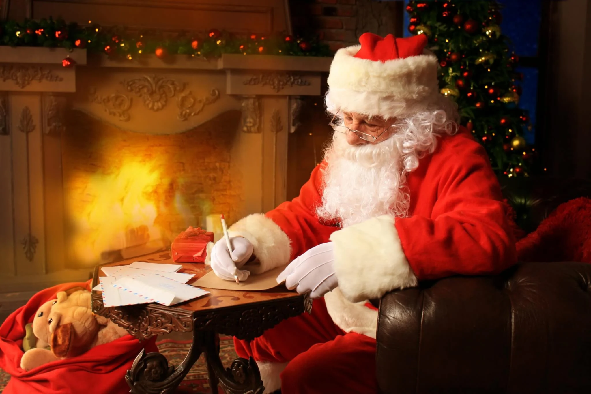 Santa writing letters in front of a fireplace